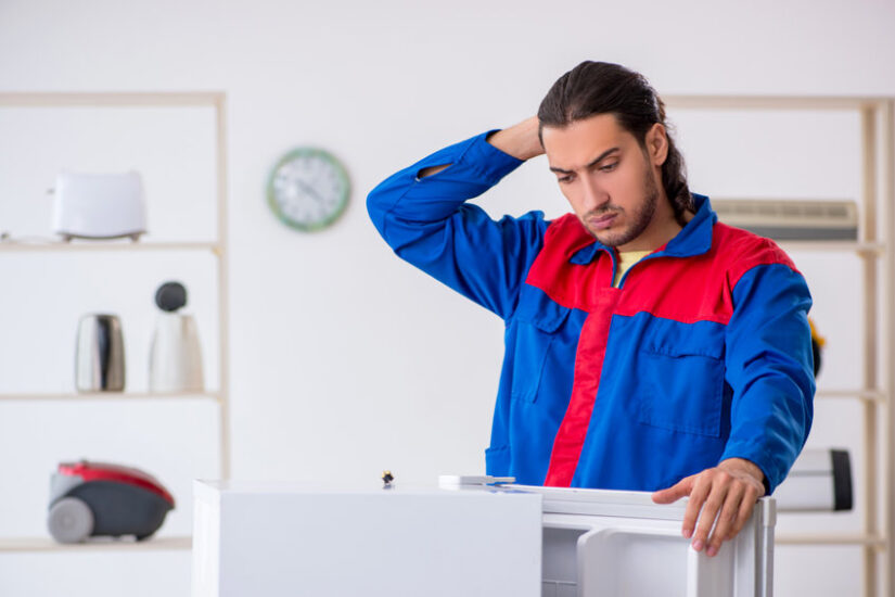 Young male contractor repairing refrigerator at workshop