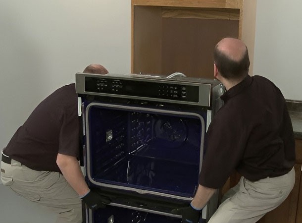 Two technicians installing a built-in wall oven safely into a cabinet